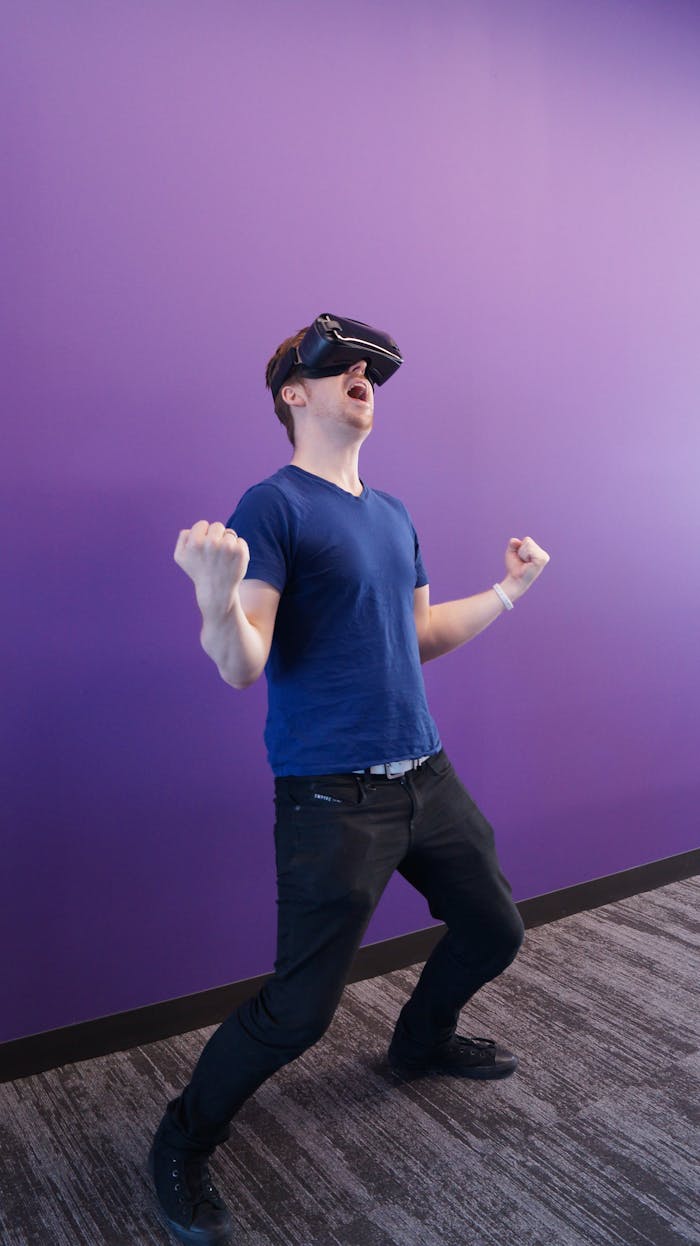 Adult male enjoying virtual reality, expressing excitement with VR headset against a purple wall.